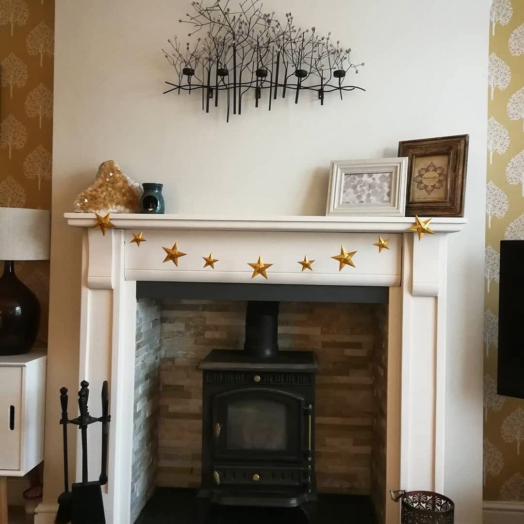 a gold origami star garland hanging from the mantelpiece of a white marble fireplace above a woodburner