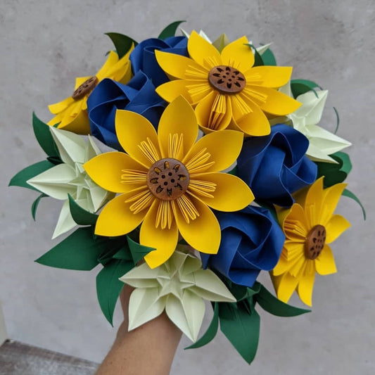 A big bridal bouquet of origami paper flowers with yellow sunflowers, royal blue roses, pale green star flowers and dark green lilies