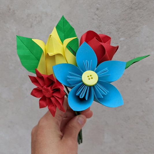 Colourful origami flower posy folded from recycled paper with a blue daisy, a red rose, a yellow tulip, a red gerbera and three green leaves