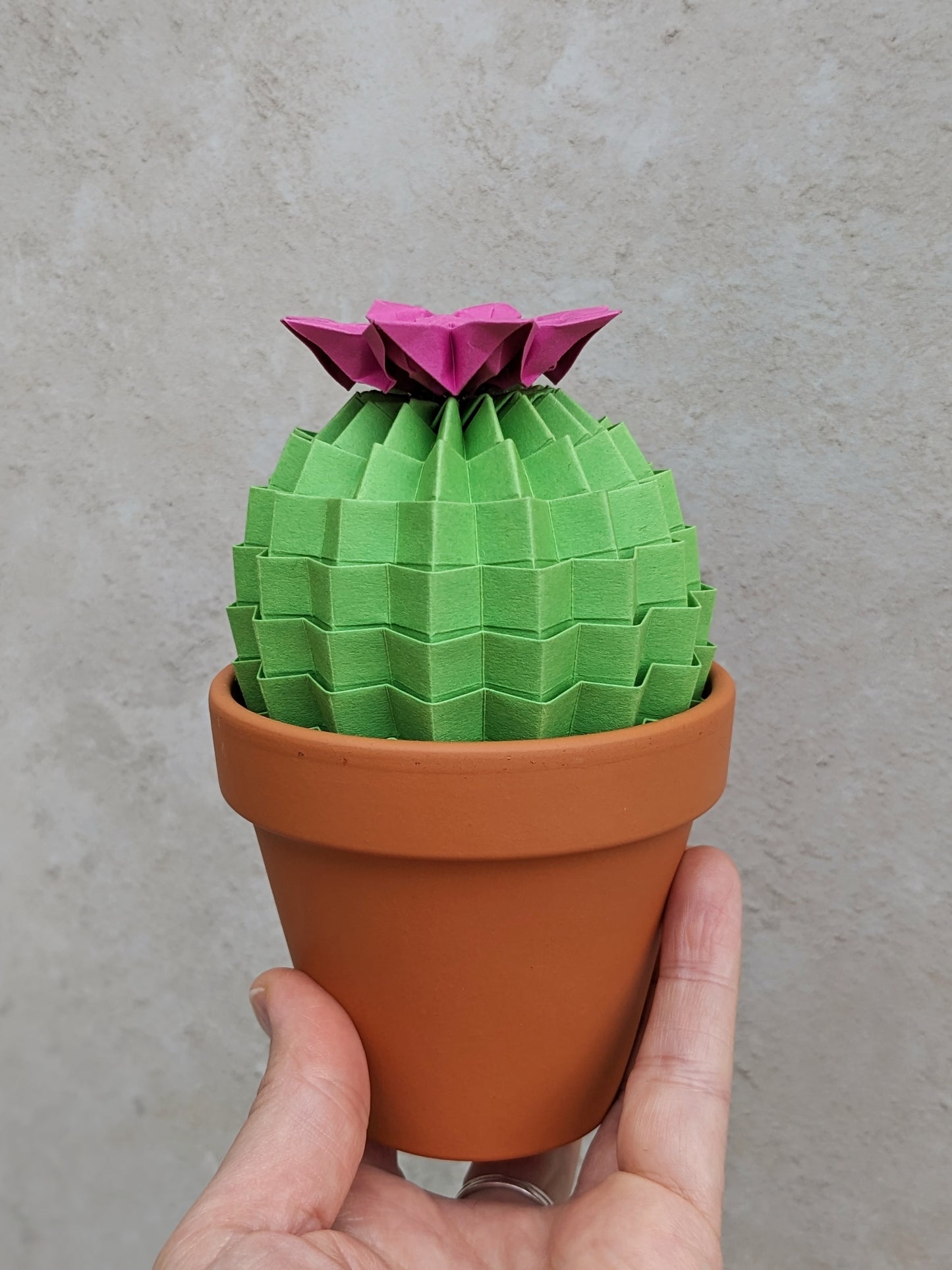 large lime green folded paper cactus with pink origami flower on top in a terracotta pot