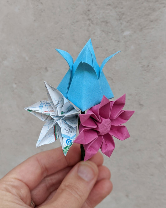 Buttonhole with recycled paper origami flowers: a blue tulip, a pink gerbera and a star flower made from an upcycled AA map