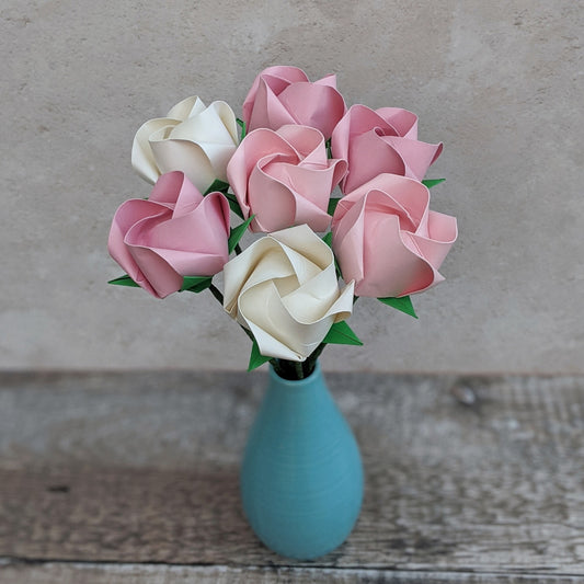 A bouquet of 7 pastel pink and ivory/off-white paper roses in a blue vase