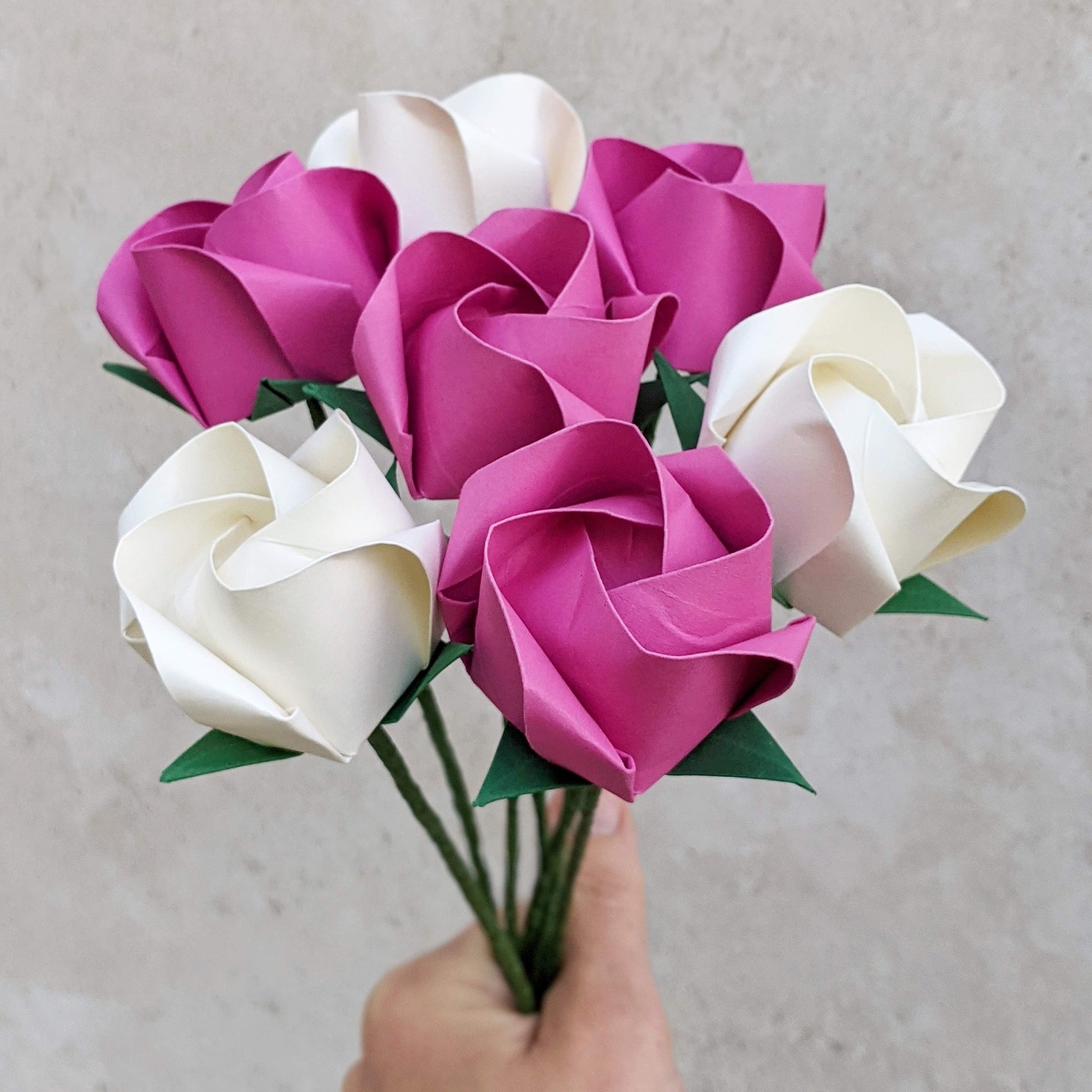 Hand holding a bouquet of seven origami paper roses, 3 white and 4 hot pink