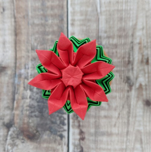 red origami paper flower with 8 petals on top of a mini green origami cactus - viewed from above