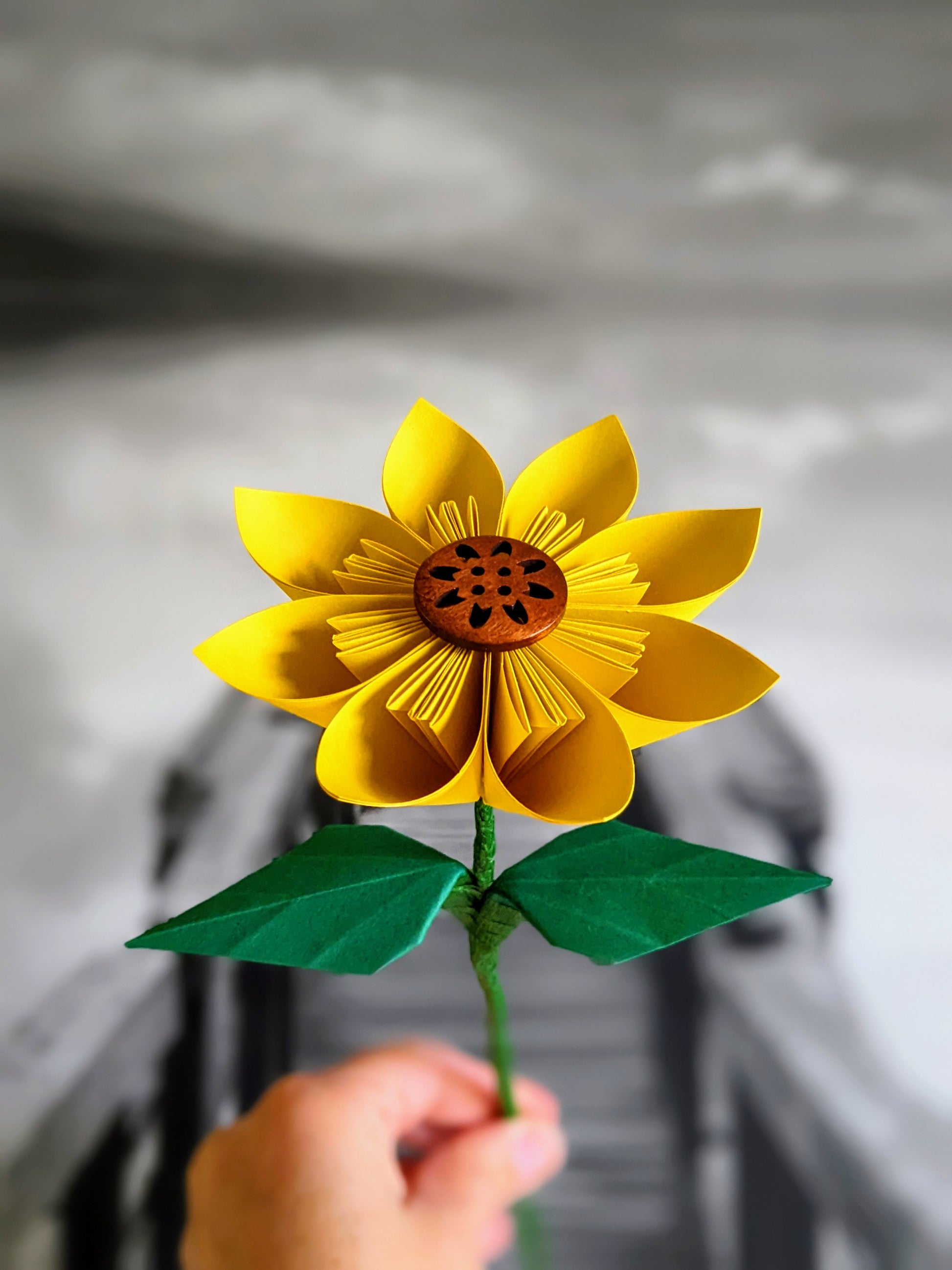 Yellow origami sunflower with 8 paper petals and a brown button centre on a long wire stem with two green leaves