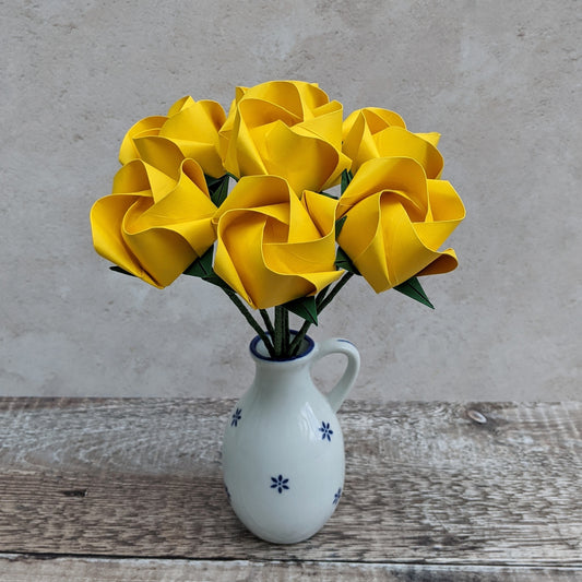 A bouquet of seven handmade origami roses folded from bright sunshine yellow recycled paper, the bouquet is in a small white vase