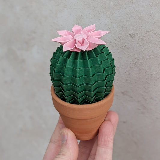 small origami cactus folded from dark green recycled paper with a pastel pink paper flower on top - in a mini terracotta pot