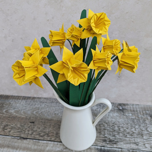 big bouquet of ten yellow origami daffodils with green leaves in a cream jug