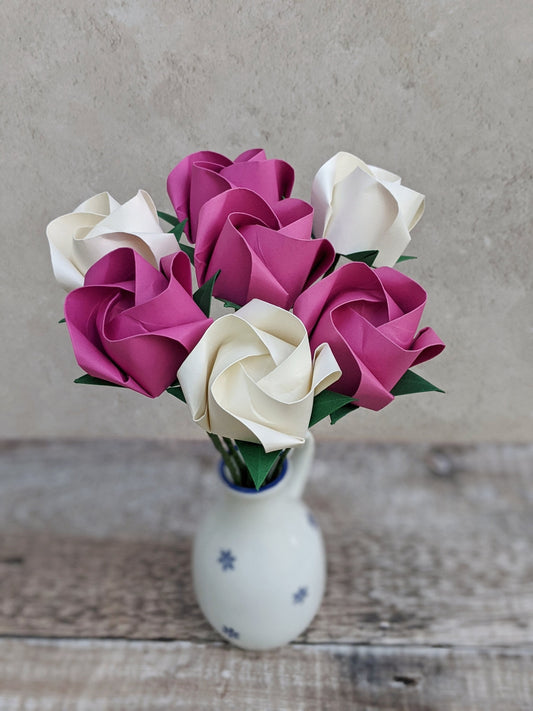 A bouquet of 7 origami roses in a small white vase. 4 roses are hot pink and 3 are ivory.
