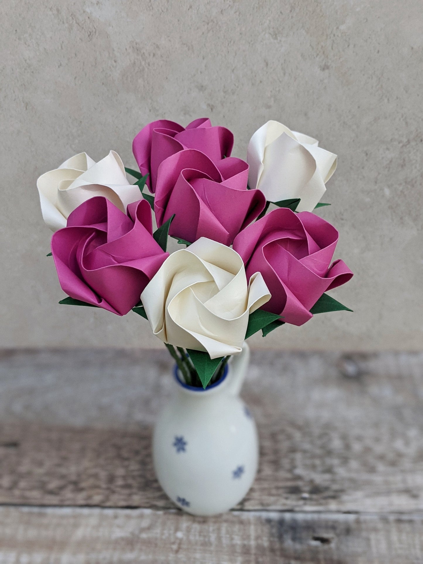 A bouquet of 7 origami roses in a small white vase. 4 roses are hot pink and 3 are ivory.
