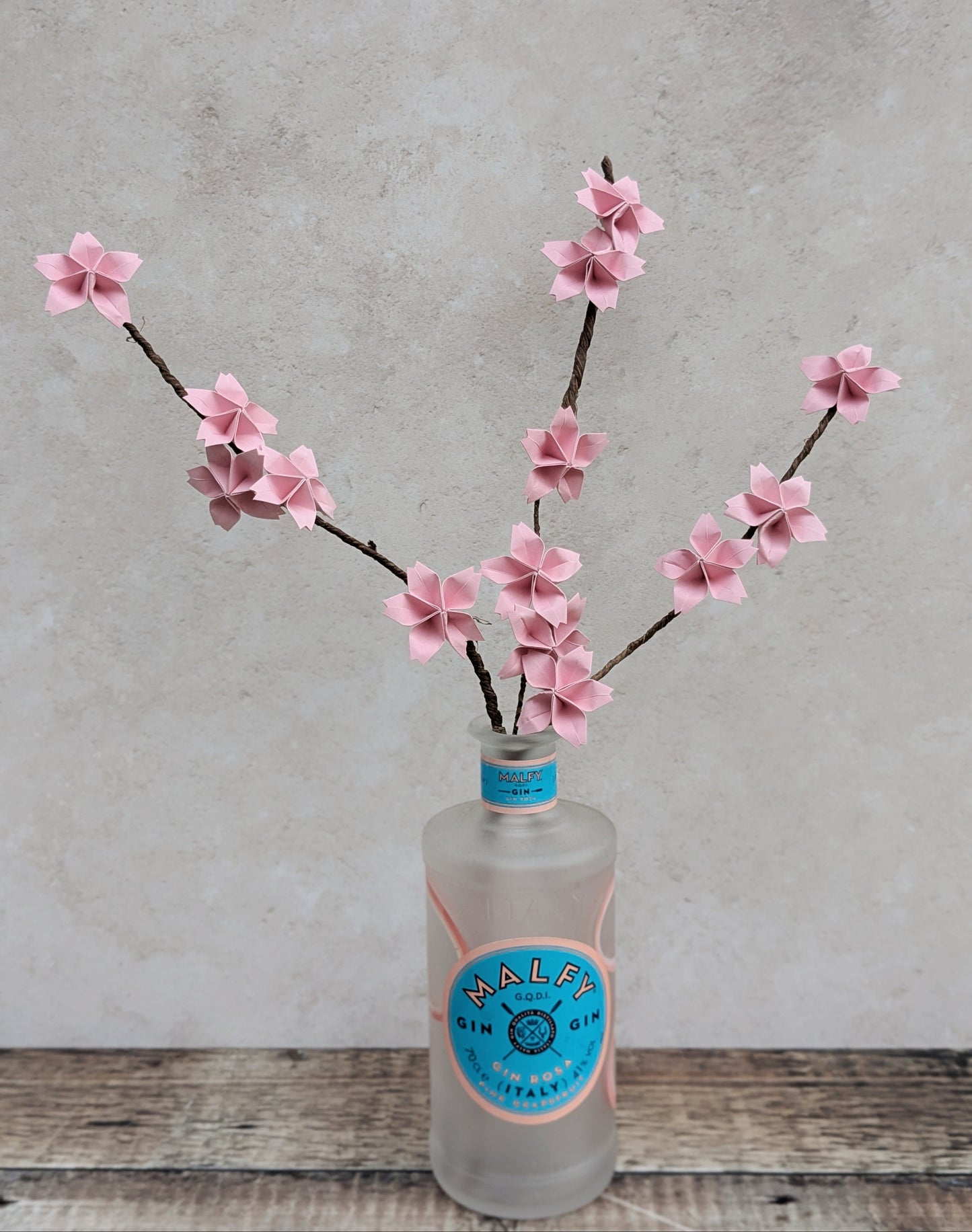 pale pink origami cherry blossom flowers on long brown stems displayed in a frosted glass bottle