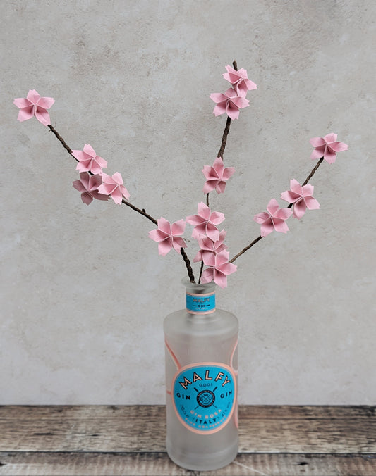 pale pink origami cherry blossom flowers on long brown stems displayed in a frosted glass bottle