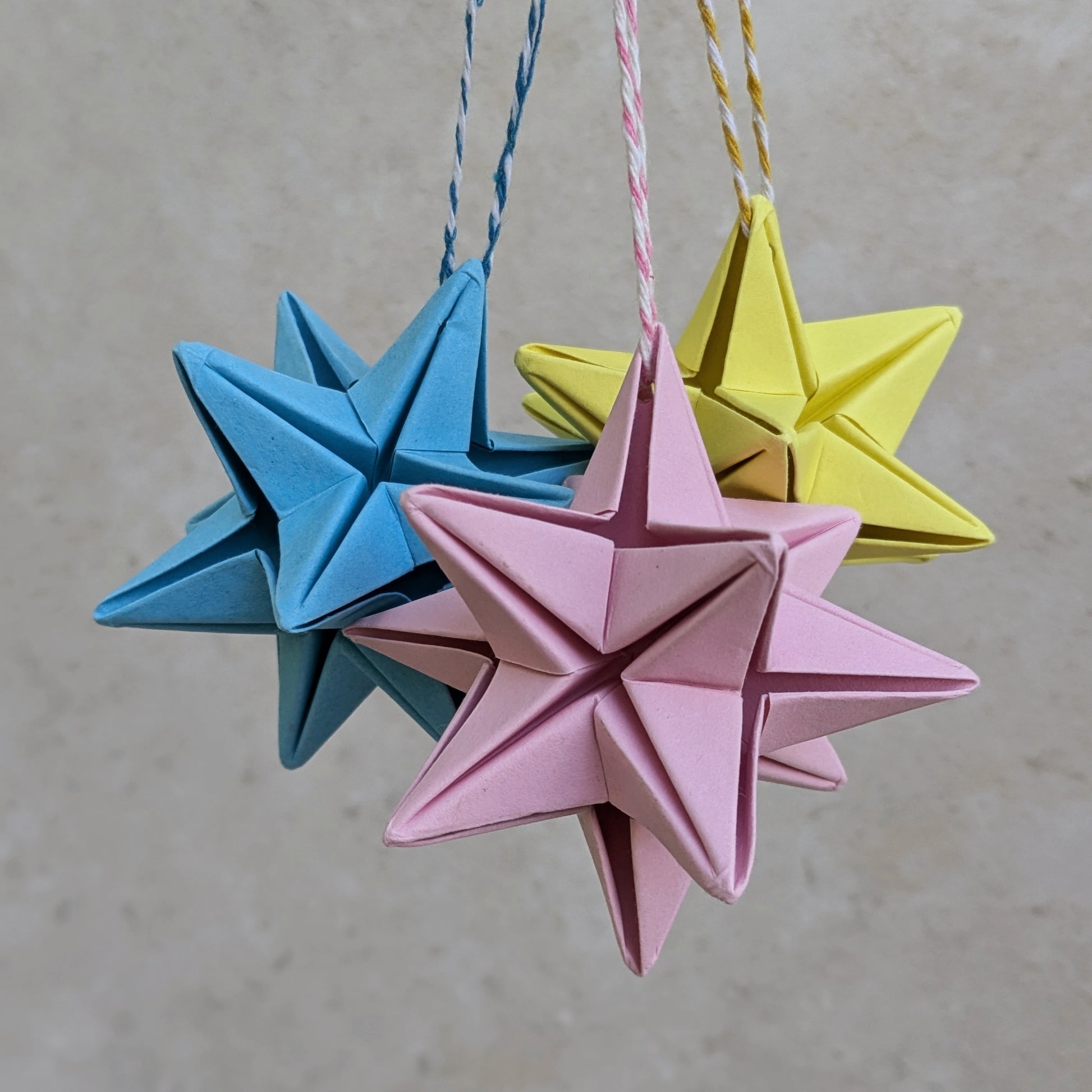 origami star baubles in pastel pink, yellow and turquoise hanging from loops of cotton twine