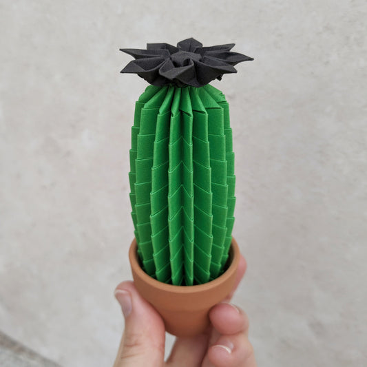 tall green origami faux cactus in a mini terracotta pot with black paper flower on top